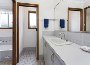Un baño con un lavamanos blanco, un espejo y una ventana con cortina.