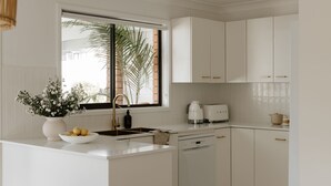 A modern kitchen with white cabinetry, a built-in dishwasher, and a window with a view of palm trees.