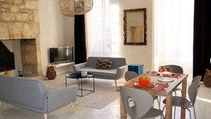 Un salon avec une cheminée en pierre, un canapé, un téléviseur et un coin repas comprenant des chaises et une table mise pour le repas.