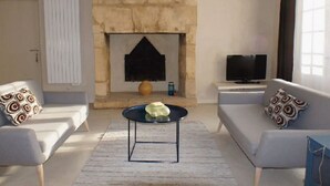 Un salon doté d’une cheminée en pierre, de deux canapés ornés de coussins à motifs, d’une table basse et d’un téléviseur à écran plat posé sur un meuble.