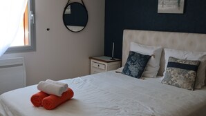 Una cama bien hecha con toallas blancas y anaranjadas, una mesita de noche con lámpara y un espejo montado en la pared.
