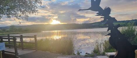 A wooden dock leading to a calm lake with a sunset in the background.