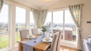 A dining area with a table set for four, large windows with curtains, and a view of the countryside. - 2 Bedroom Sleeps 4 Lodge-smart Tv-hot Tub-dogs Ok (Lochwinnoch)