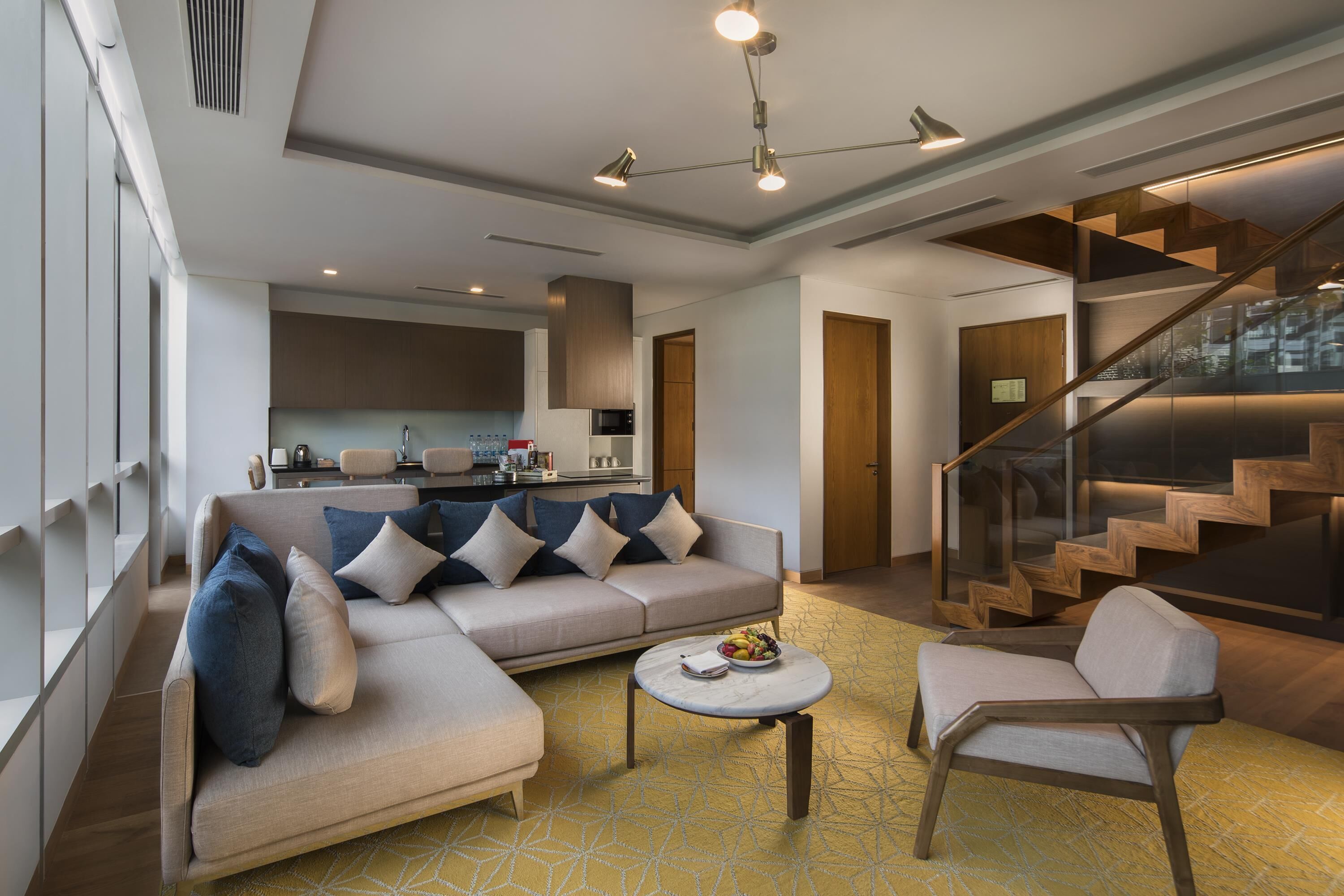 A modern living room with a sofa, armchairs, a coffee table, and a staircase.
