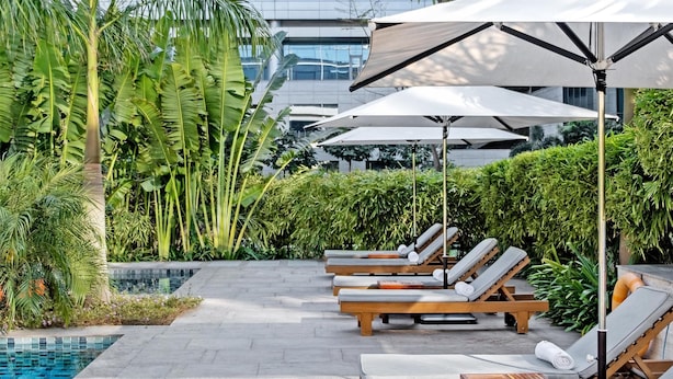A poolside area with lounge chairs and umbrellas, a modern building in the background, and a clear sky. - Hyatt Delhi Residences (New Delhi)