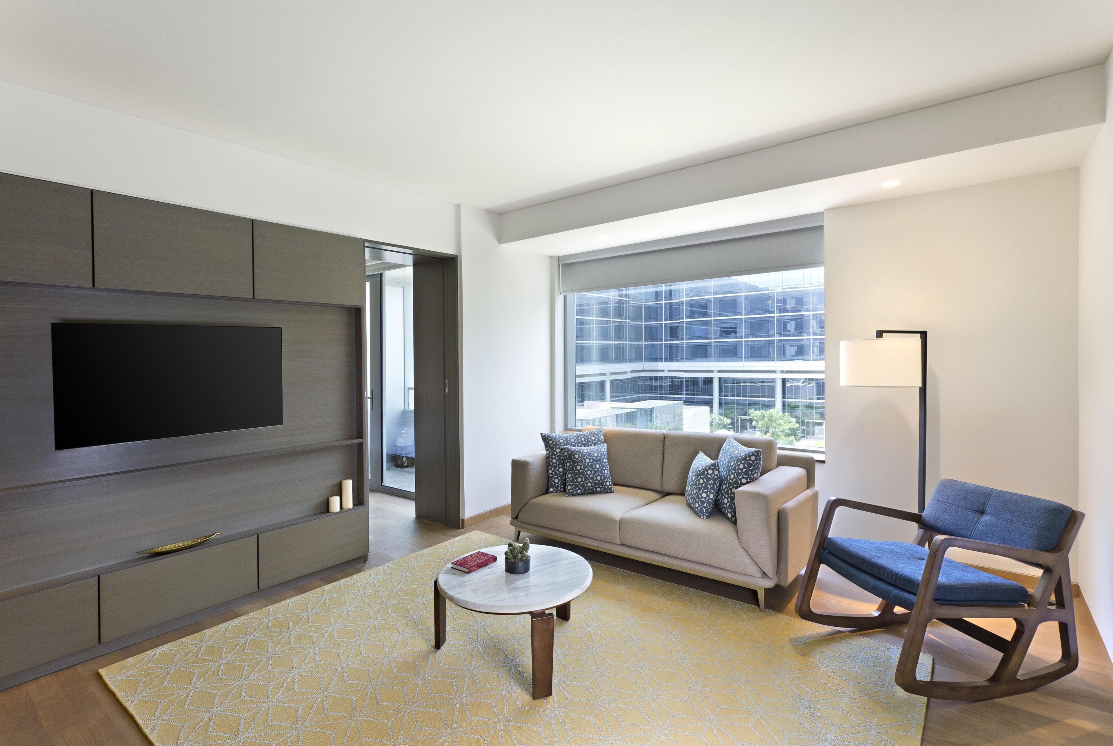 A modern living room with a flat-screen TV, a sofa, a rocking chair, and a patterned rug.