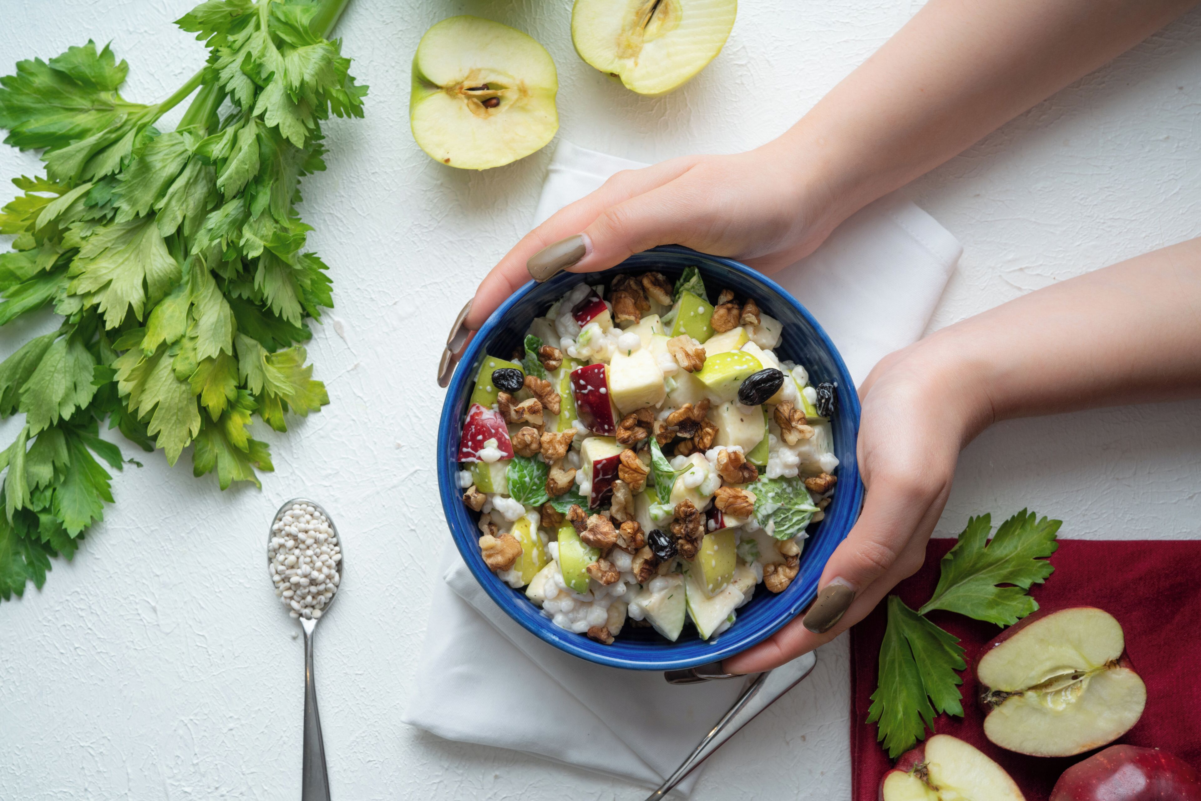A bowl of fruit salad with nuts and a spoon on a white surface.