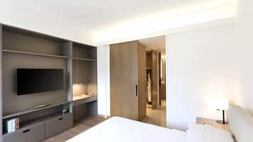 A modern hotel room with a flat-screen TV, a bedside table with a lamp, a large bed, and a wardrobe with a mirror.