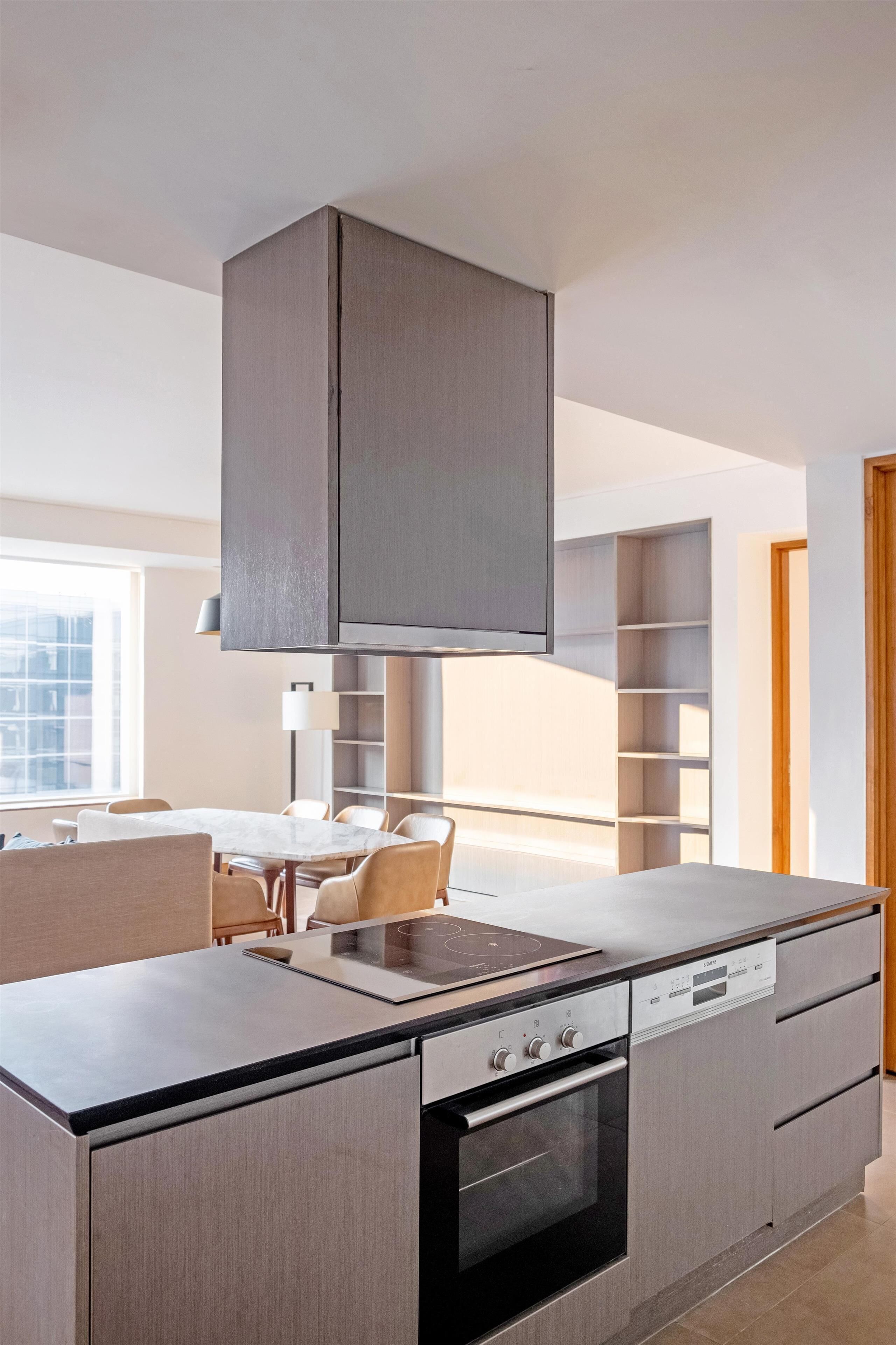 A modern kitchen with a built-in oven, a dining area with a table and chairs, and a large window providing natural light.