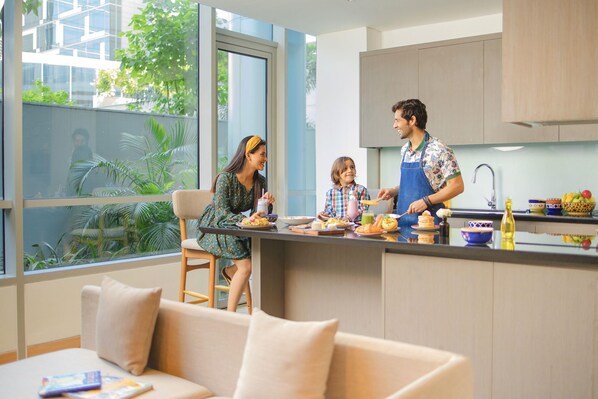 A modern kitchen with a large window, a dining area with a sofa, and a child preparing food.