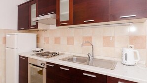 Una cocina con armarios de madera oscura, encimera blanca, pileta de acero inoxidable y hervidor eléctrico blanco.