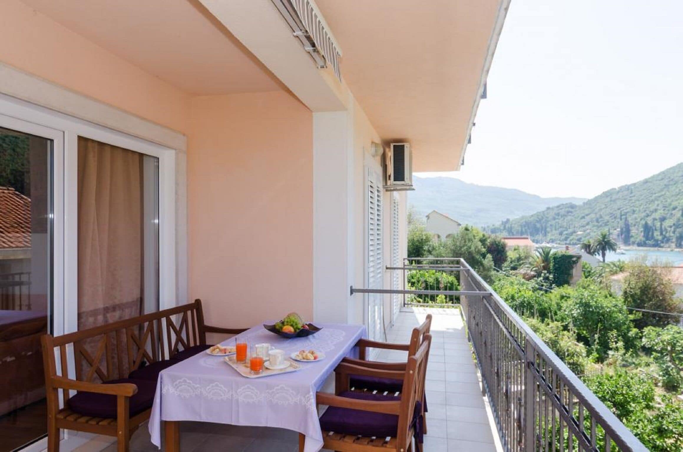 Un balcón con una mesa dispuesta para el desayuno, con vistas a un paisaje pintoresco de montañas y una masa de agua.