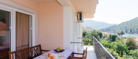 Un balcón con una mesa dispuesta para el desayuno, con vistas a un paisaje pintoresco de montañas y una masa de agua.