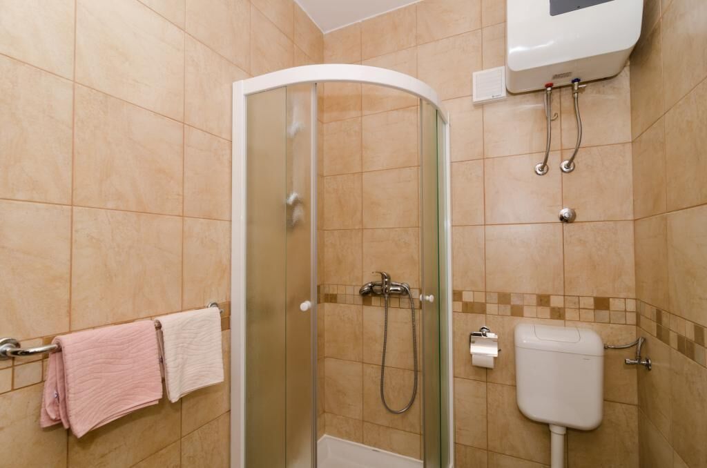 A bathroom with a glass-enclosed shower, a toilet, and a towel rack with pink and white towels.