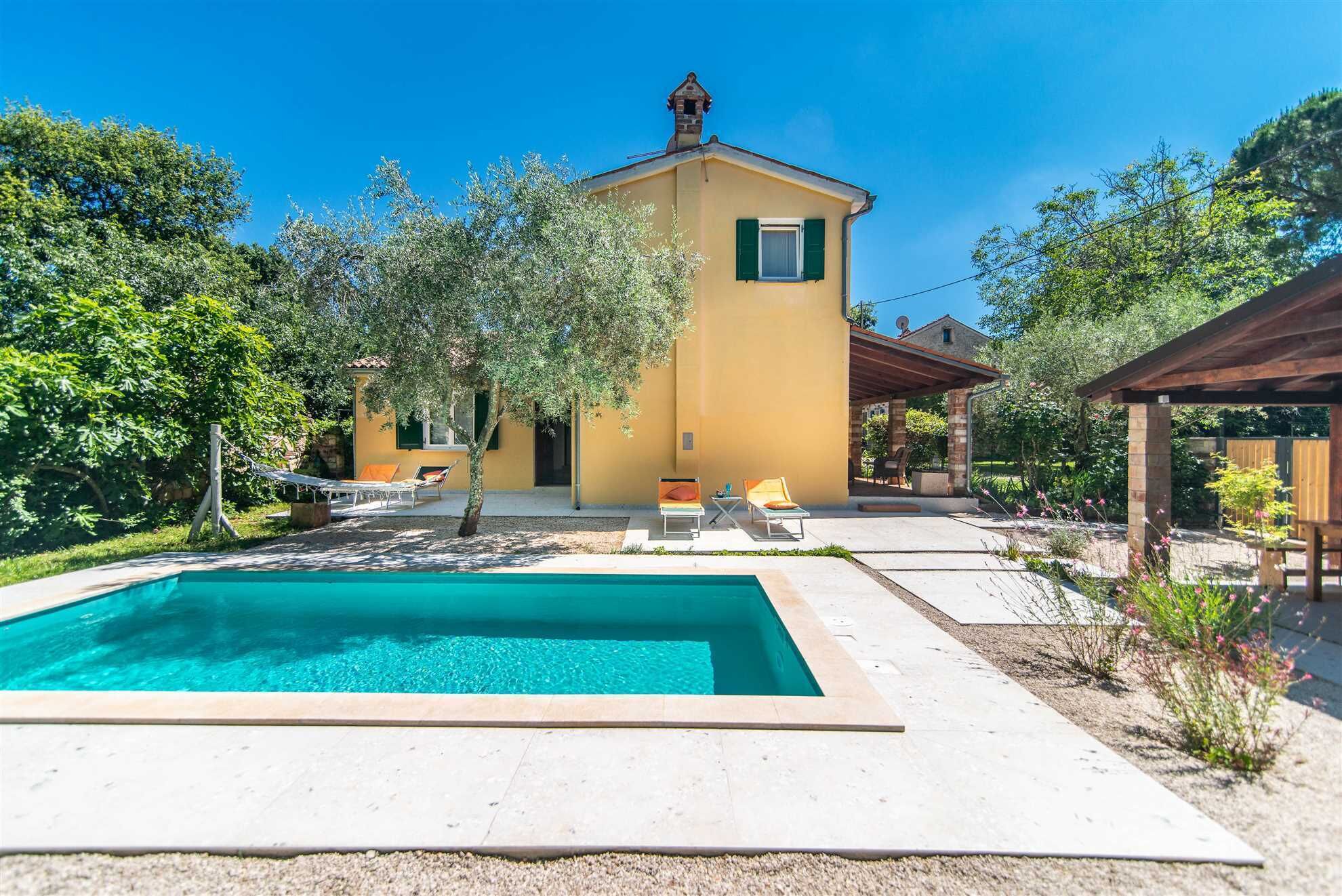 A yellow villa with a swimming pool, outdoor seating, and a garden.