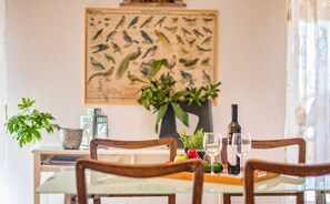 Uma mesa de jantar com cadeiras, tampo de vidro, uma garrafa e um copo de vinho.
