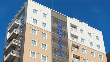 A multi-story hotel with a beige and white facade, balconies, and a clear blue sky.