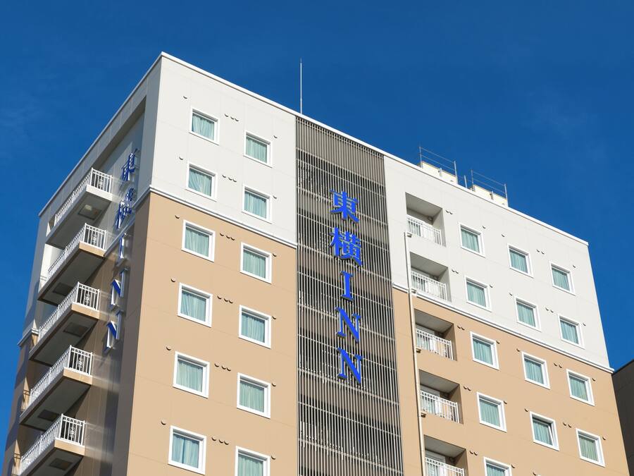 A multi-story hotel with a beige and white facade, balconies, and a clear blue sky.