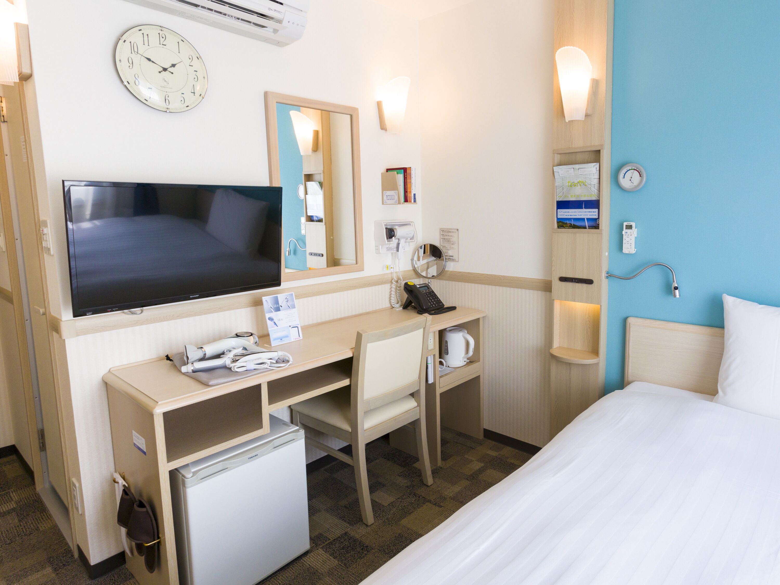 Une chambre d’hôtel comprenant un lit, un bureau avec une télévision, un réfrigérateur, une machine à café, un téléphone et un miroir.