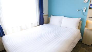 A hotel room with a large bed, a bedside table with a lamp, a wall clock, and a window with curtains.