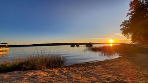Un lac paisible au coucher du soleil, avec des bateaux et une plage de sable.