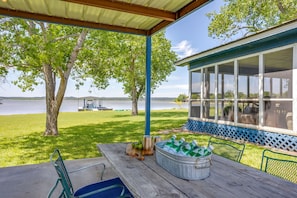 A covered patio with a view of a lake, a table with a bucket of bottles, and a covered seating area.