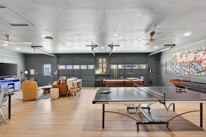 A spacious room with a ping pong table, ceiling fans, and a large window.