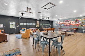 A spacious room with a wooden dining table, light blue chairs, a pool table, and a colorful mural on the wall.