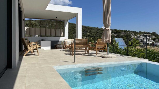 Un espace piscine extérieur moderne offrant une vue dégagée sur la mer et les collines en arrière-plan.