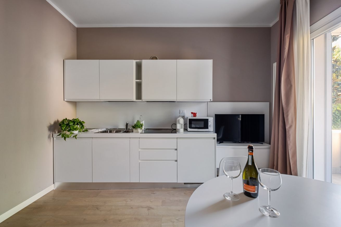 Une cuisine moderne avec des meubles blancs, un four à micro-ondes et une bouteille de vin posée sur le plan de travail.