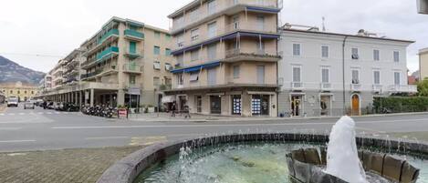 A public square with a fountain, buildings, and a street.