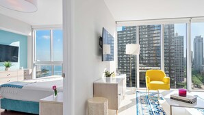 A modern bedroom with a large bed, a desk, a yellow armchair, and a view of tall buildings. - Modern 2BR Apartment | Steps to Brickell City Centre (Miami)
