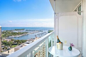 A balcony with a view of a marina, a table with a bottle of champagne, and a glass of wine.