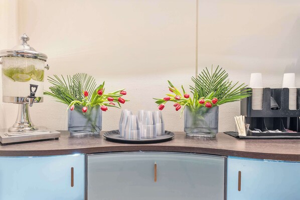 A bar area with a coffee machine, glassware, and decorative vases with red flowers.