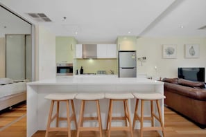 Una cocina moderna con una isla central, taburetes de bar, un sofá y una televisión.