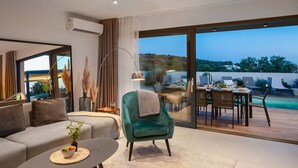 A modern living room with a sofa, armchair, dining table, and a view of a swimming pool. - Luxury Villa Indigo Kanica with Heated Pool (Dvornica)