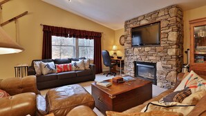Un salón acogedor con chimenea de piedra, muebles de cuero y un televisor montado en la pared.