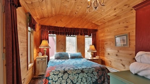 Un dormitorio de cabaña de madera acogedor, con una cama grande, dos lámparas de noche, una araña y un ventanal con cortinas.