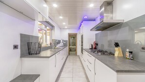 Cozinha moderna com armários brancos, coifa de aço inoxidável e bancada cinza.
