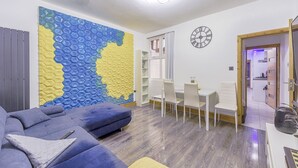 Uma sala de estar moderna com um sofá azul, um cobertor amarelo e uma peça de arte hexagonal na parede.