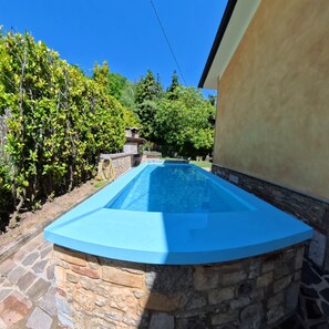Une piscine bordée d’un muret en pierre et dotée d’un escalier en pierre menant à une zone abritée.