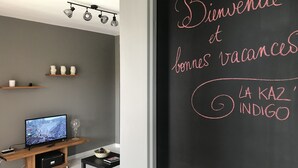 Un salon moderne avec une télévision, des étagères et un tableau noir sur lequel est écrit un message de bienvenue.