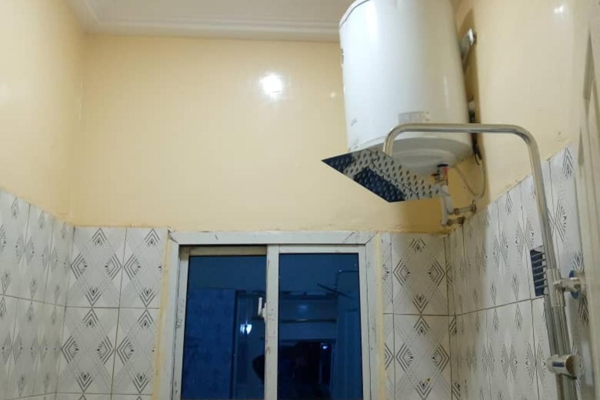Een badkamer met een douche, een raam en betegeling met een patroon.