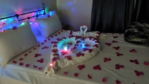 A bed with rose petals and a heart-shaped arrangement of towels, illuminated by colored lights. - 4 Bed House Sleeps 8 - Garden and Pets Welcome (Brikama)