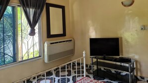 A room with a large window, air conditioning unit, a flat-screen TV on a stand, and a staircase with a railing. - 4 Bed House Sleeps 8 - Garden and Pets Welcome (Brikama)