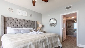Une chambre à coucher avec une tête de lit capitonnée, un grand lit avec une literie à rayures, deux appliques murales et un miroir.
