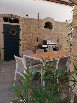 Eine Terrasse im Freien mit einer Steinmauer, einem Holztisch und weißen Stühlen.