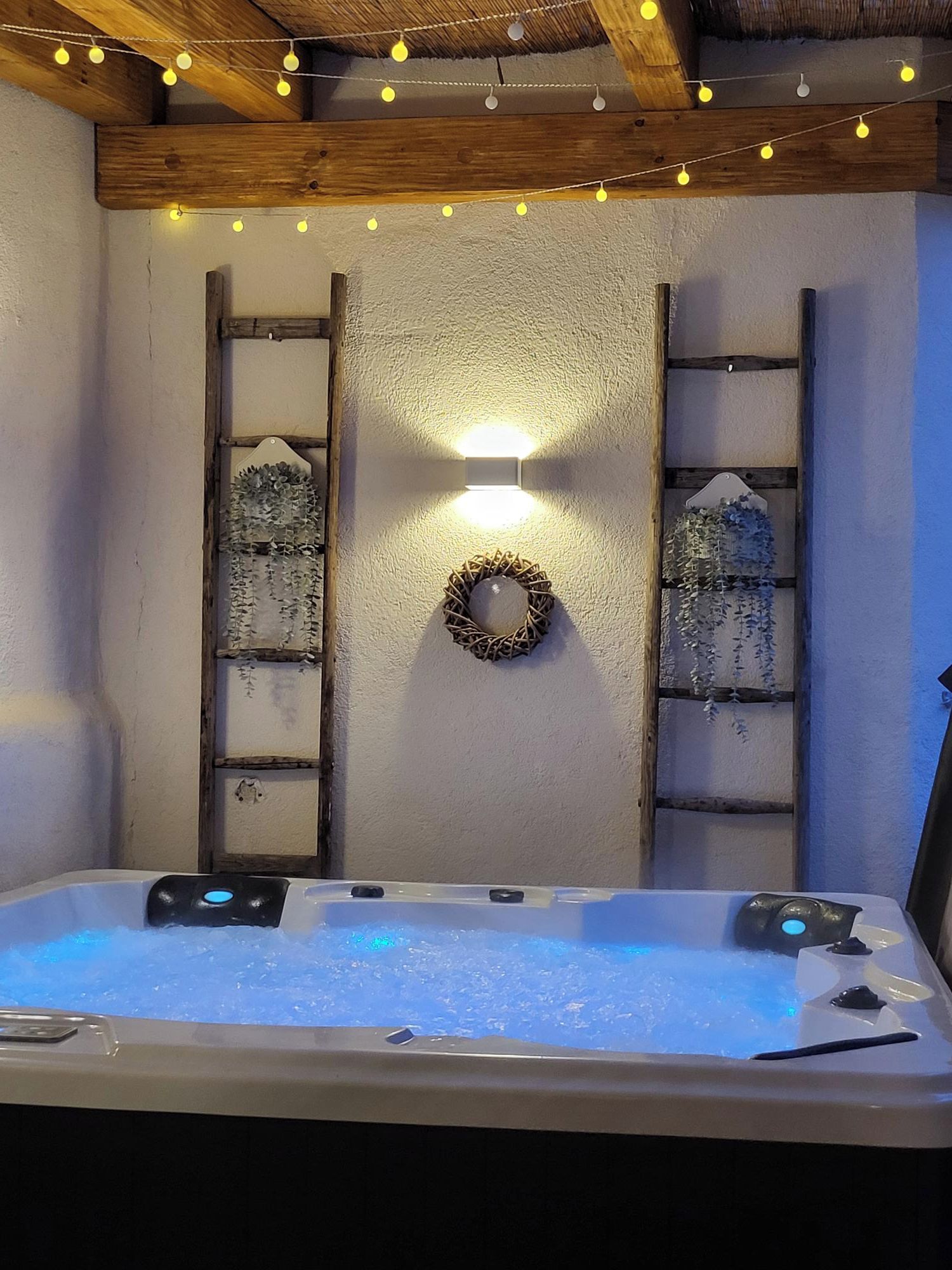 A hot tub with a light fixture above it, surrounded by wooden beams and a textured wall.