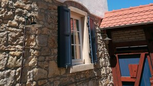 Un edificio con fachada de piedra, una ventana con contraventanas azules y un cielo azul despejado.