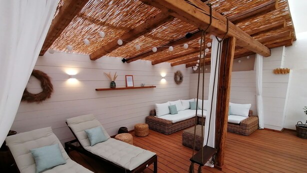 Un espacio al aire libre acogedor con suelo de madera, sillones lounge acolchados y una silla colgante.